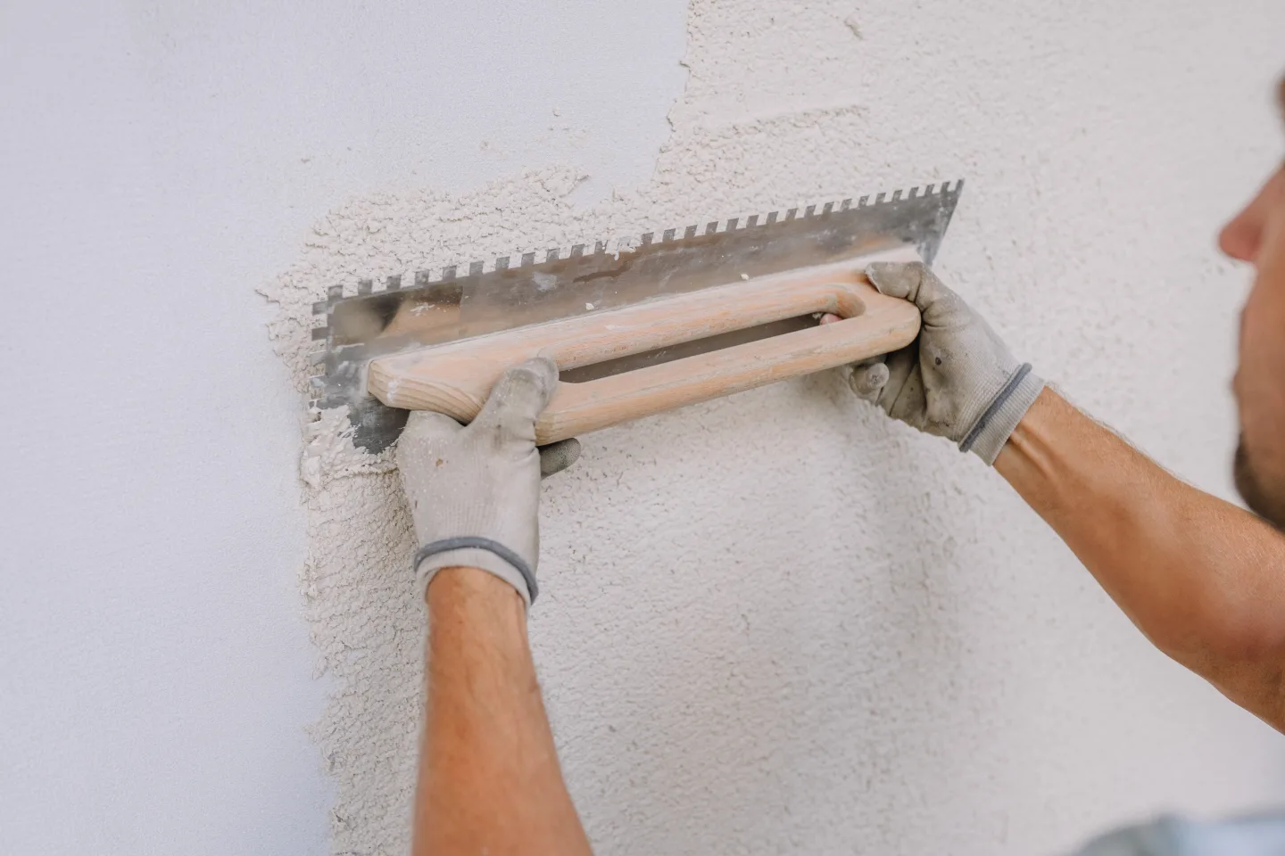Ein Arbeiter glättet Gips an einer Wand mit einer gekerbten Kelle mit Kalkputz.