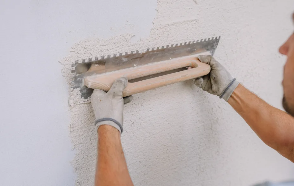 Ein Arbeiter glättet Gips an einer Wand mit einer gekerbten Kelle mit Kalkputz.